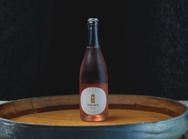 Bimbadgen Sparkling Moscato NV bottle with pink hue displayed on barrel in cellar setting