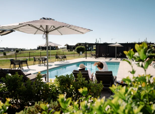 Two guests relaxing on sun loungers beneath an umbrella beside the outdoor pool at The Lane Retreat.