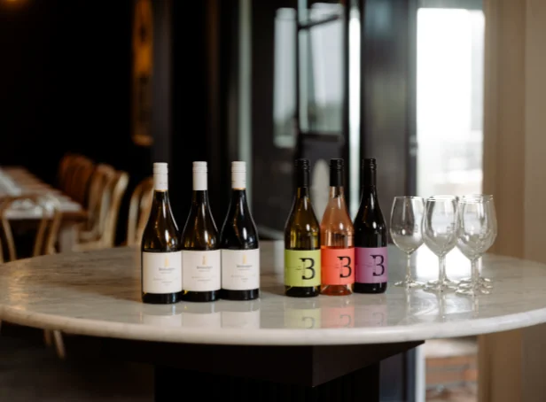 Six Bimbadgen wine bottles and a selection of empty wine glasses displayed on a round marble table at the cellar door.