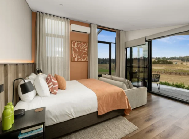 Studio Retreat interior with a king bed, peach throw, sofa and sliding glass doors opening towards vineyard views.